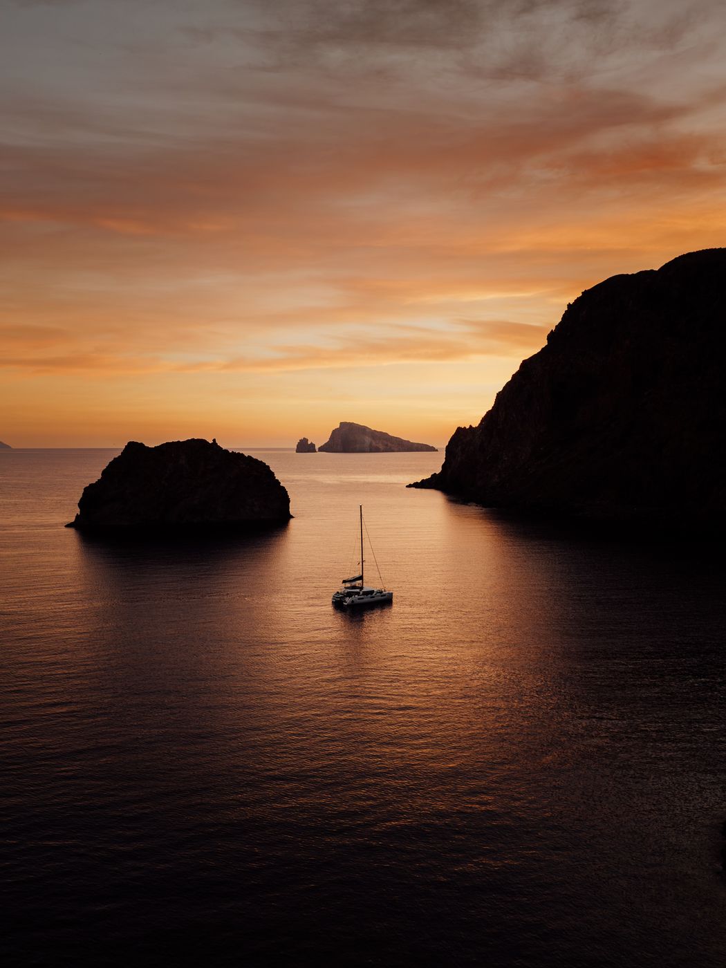 Catamaran at anchor at sunset between two islands